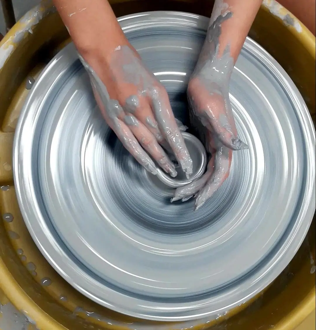 top down view of a spinning pottery wheel with hands cupping a clay bowl