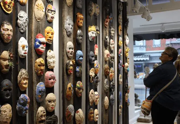 woman looking up at clay masks displayed on wood boards
