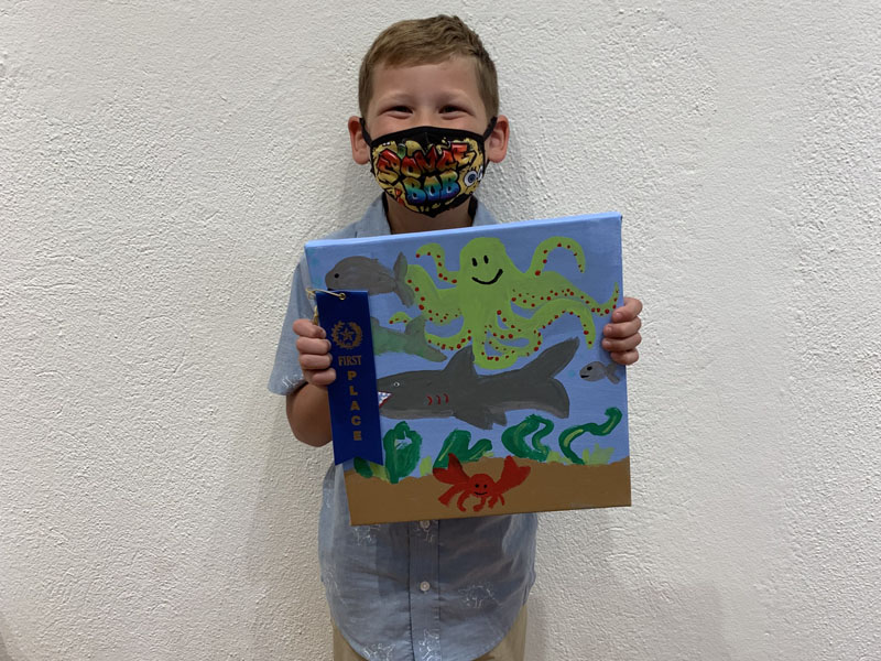 young child holding artwork and ribbon