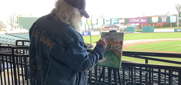 man painting outside at baseball stadium