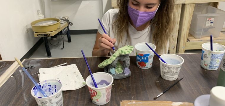 child glazing a pottery project with a variety of different colors