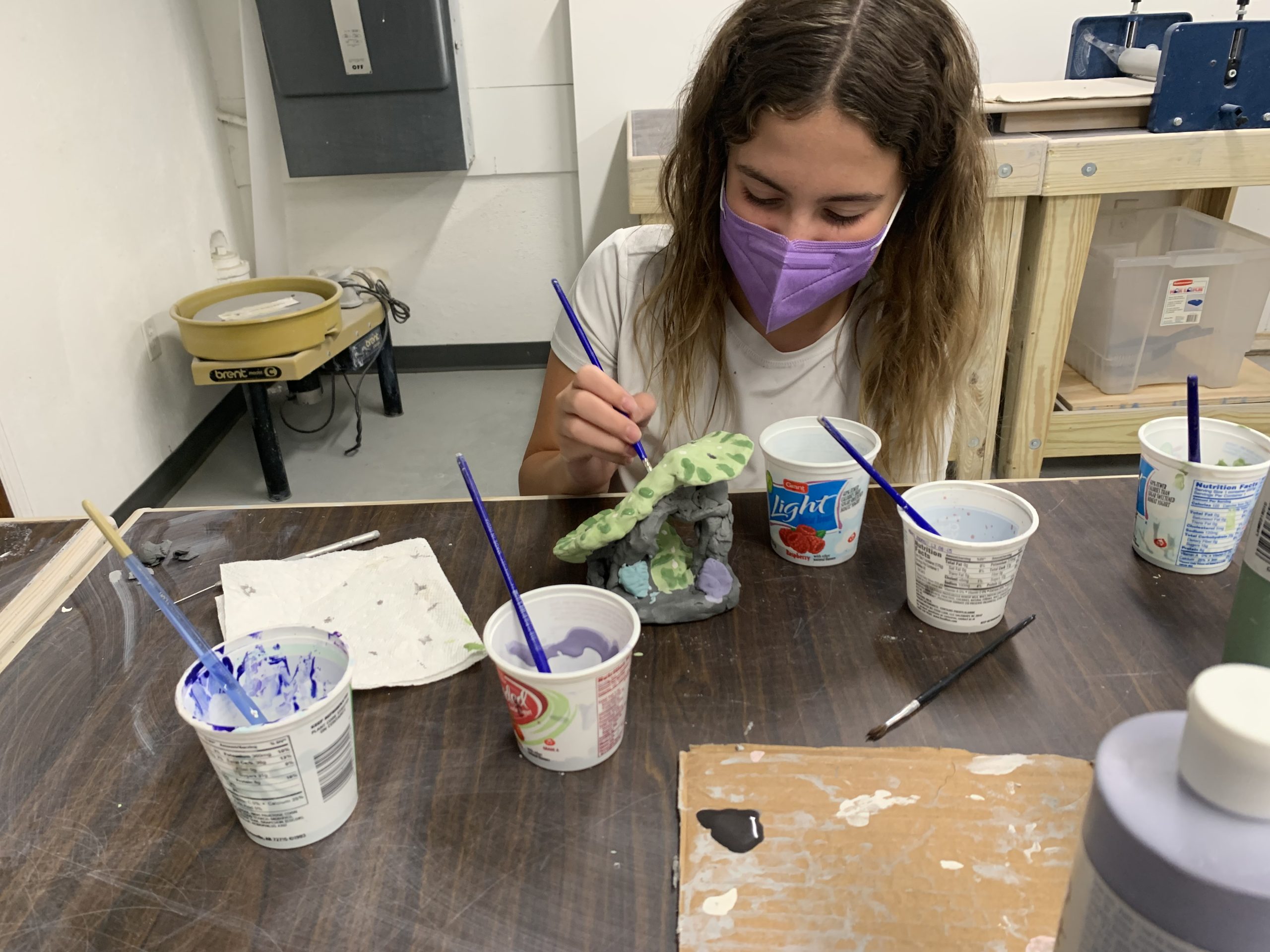 child glazing a pottery project with a variety of different colors