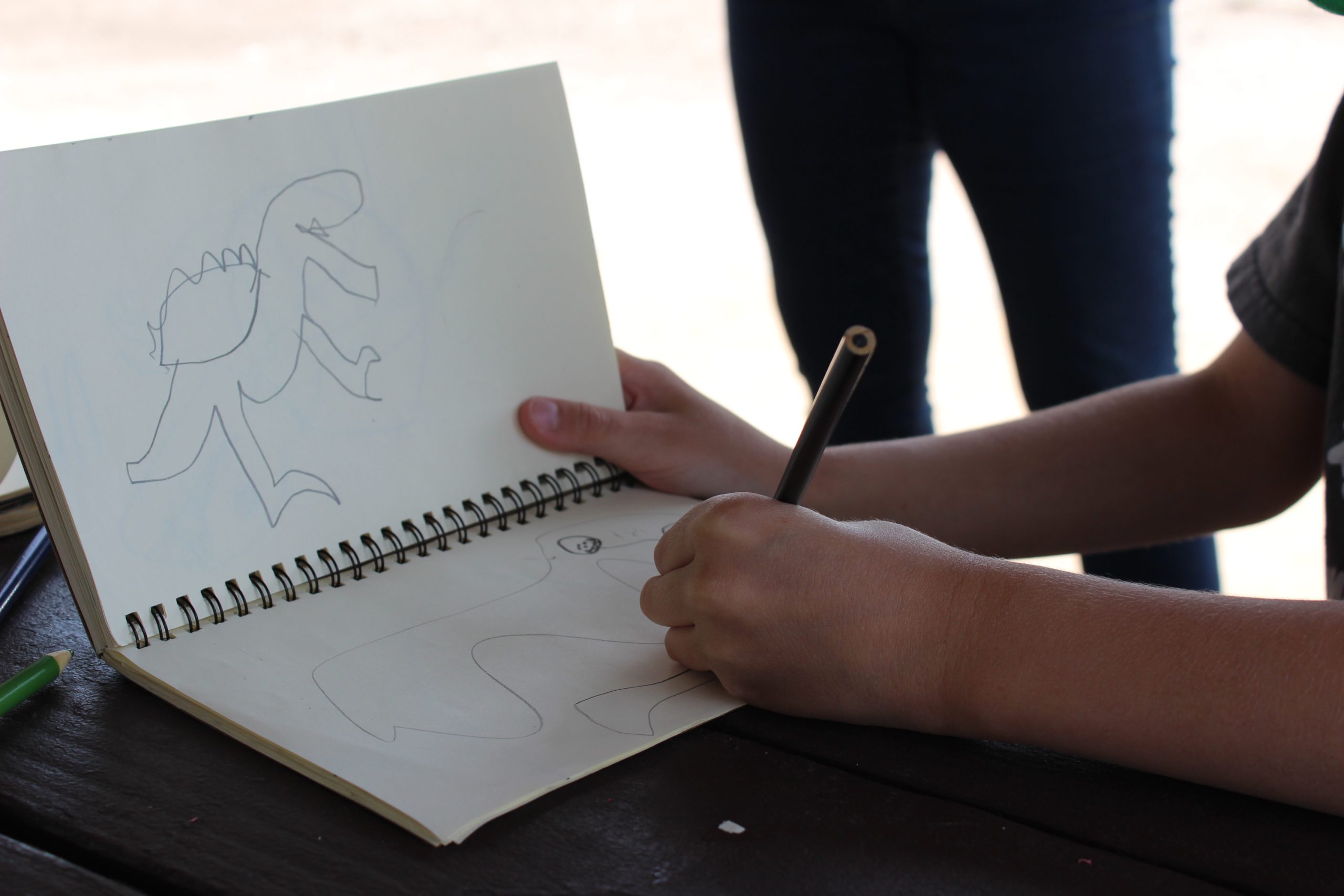 child holding a colored pencil while drawing in an open sketchbook