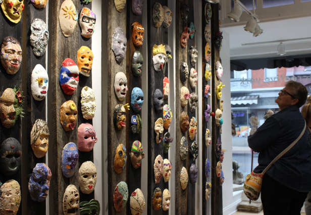 woman looking up at clay masks displayed on wood boards