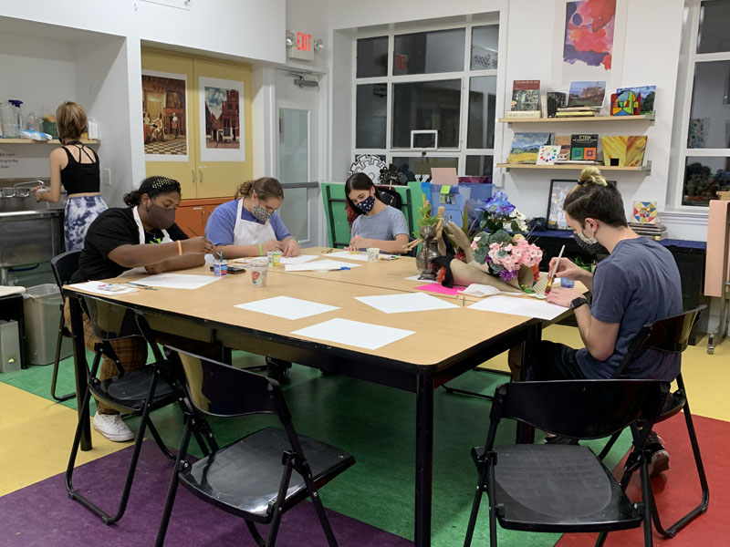 students sitting at table painting still life sculpture