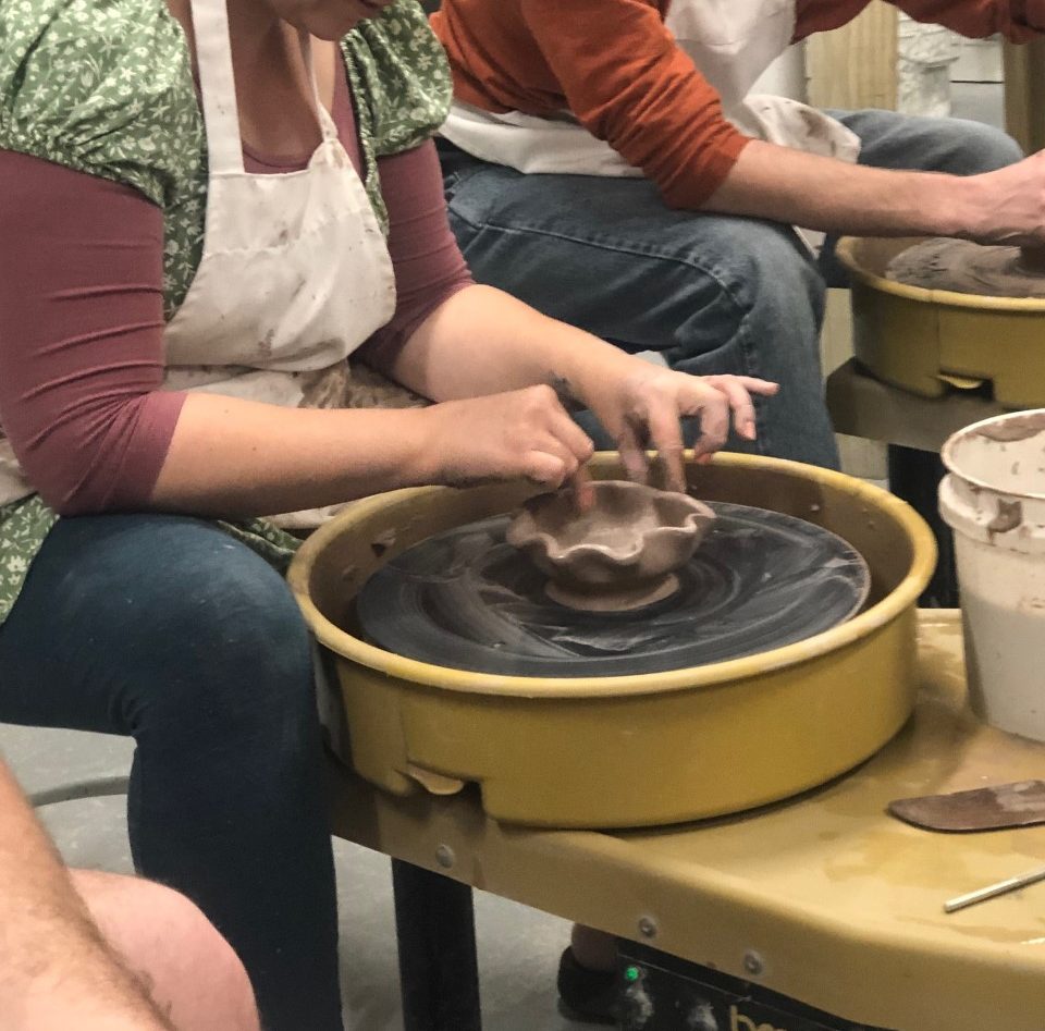 person molding a bowl on a pottery wheel